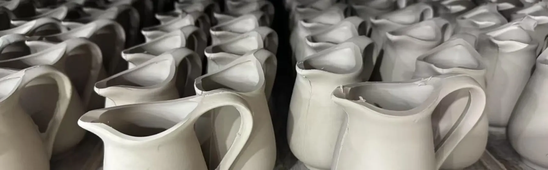 Unfired stoneware pitchers drying in rows at a Vietnam ceramic factory