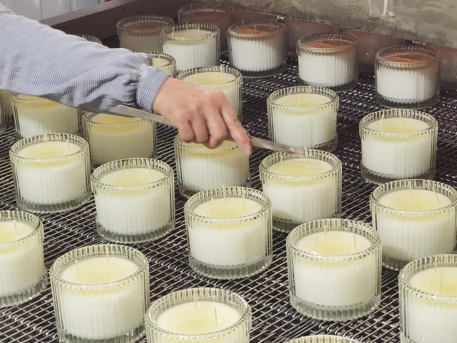 Hand finishing candles in ribbed glass jars on a curing rack