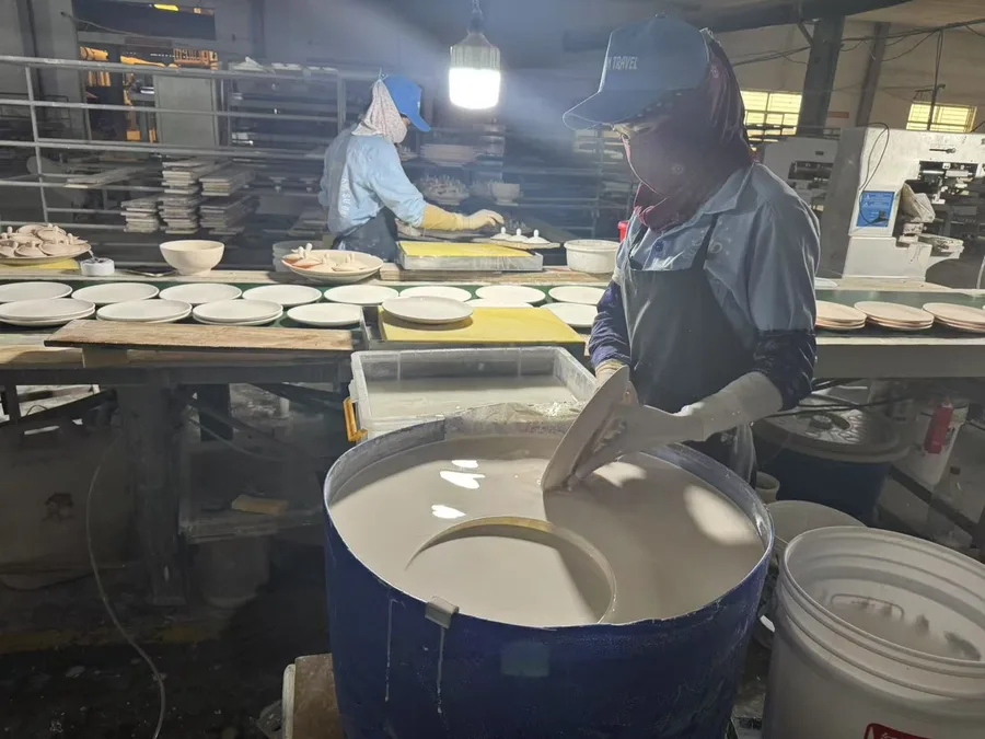 A stoneware plate being dip-glazed by hand